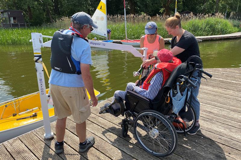 Hoist process step 1 - the sailor has arrived already sitting on the sling (see black fabric hanging over back of wheelchair) and the spreader bar can be attached photo copyright Magnus Smith taken at Frensham Pond Sailability and featuring the Dinghy class