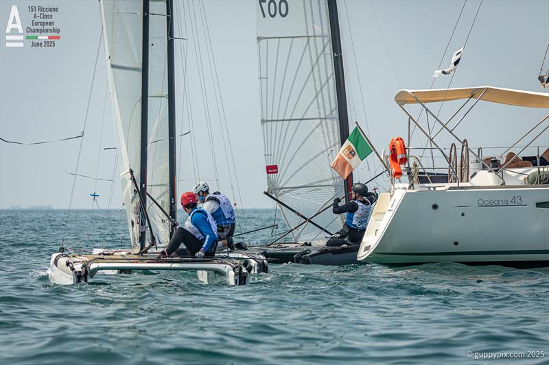 Like naughty shoolboys and girls, the boats who were too far from the line as the sequence started sneak around the stern of the committee boat, 5 mins late - A-Class Cat European Championships at Riccione Day 3 - photo © Gordon Upton / www.guppypix.com