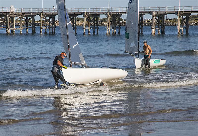 The legend that is Anthony 'Nocka' Nossiter with his Finn on the dolly as Olympian Jake Lilley also comes ashore after training. - photo © John Curnow